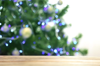 Photo of Blurred view of fir tree with glowing Christmas lights near table indoors. Festive mood