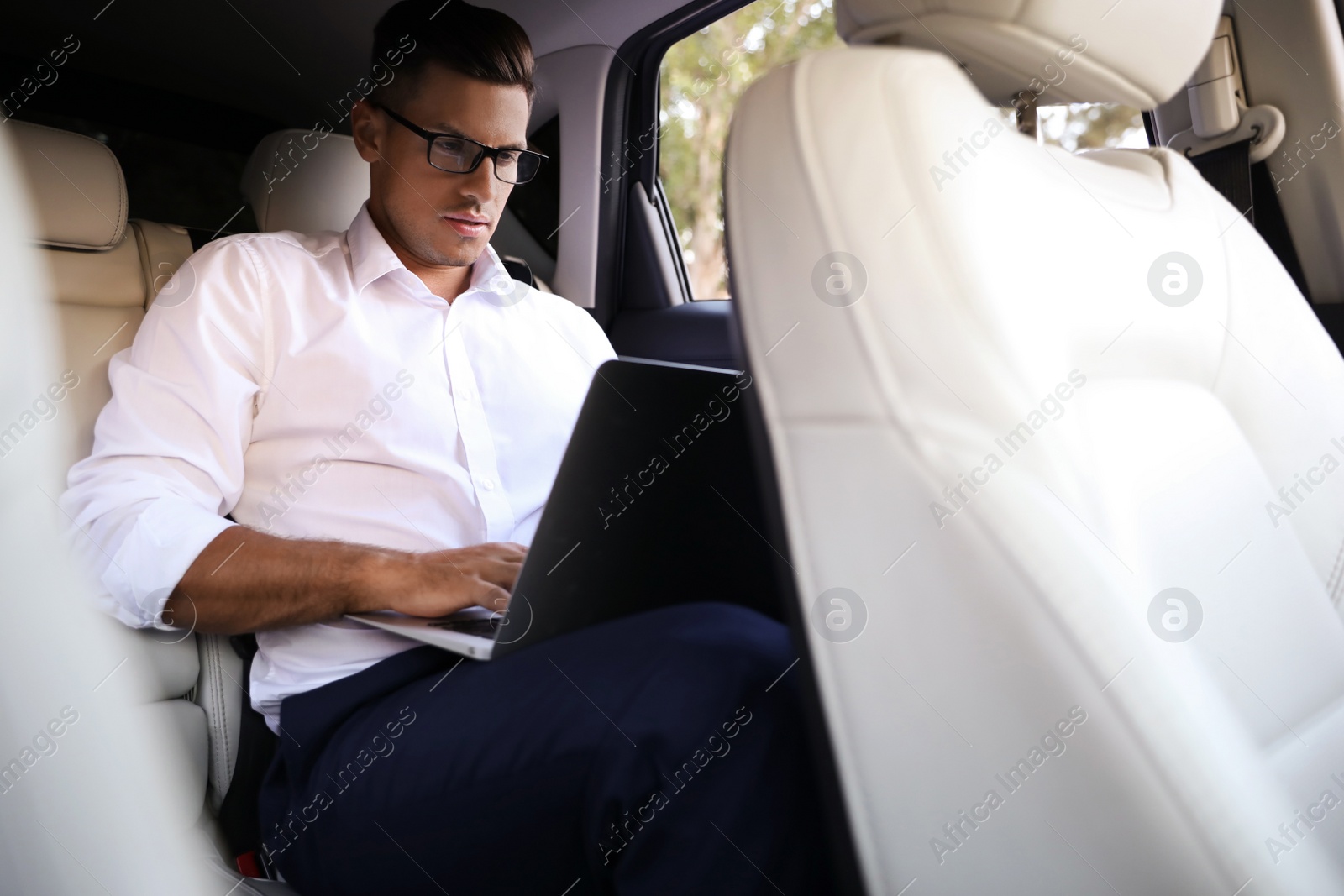 Photo of Handsome man working with laptop on backseat of modern car