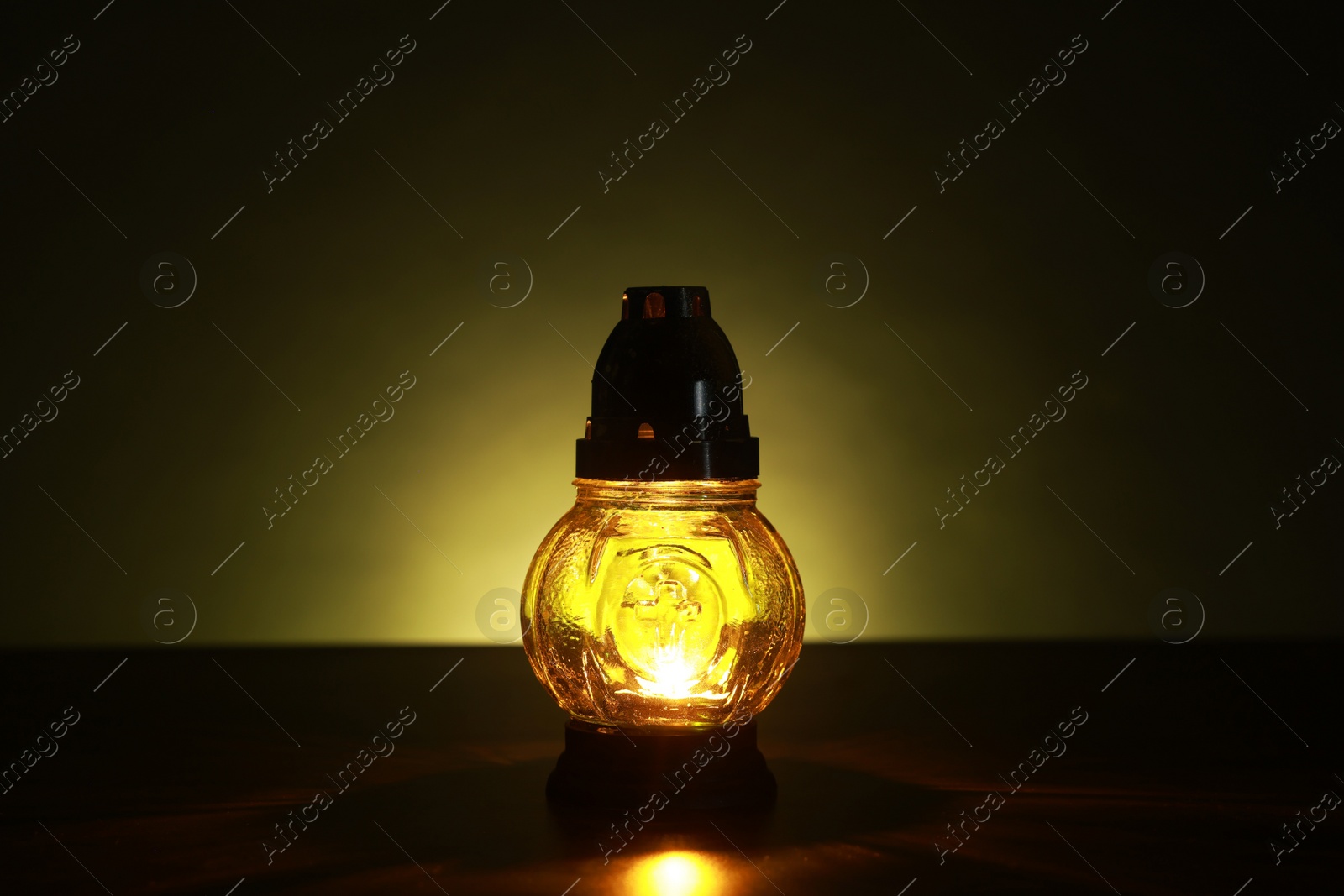 Photo of Beautiful glowing yellow grave light on table in darkness. Symbol of remembrance