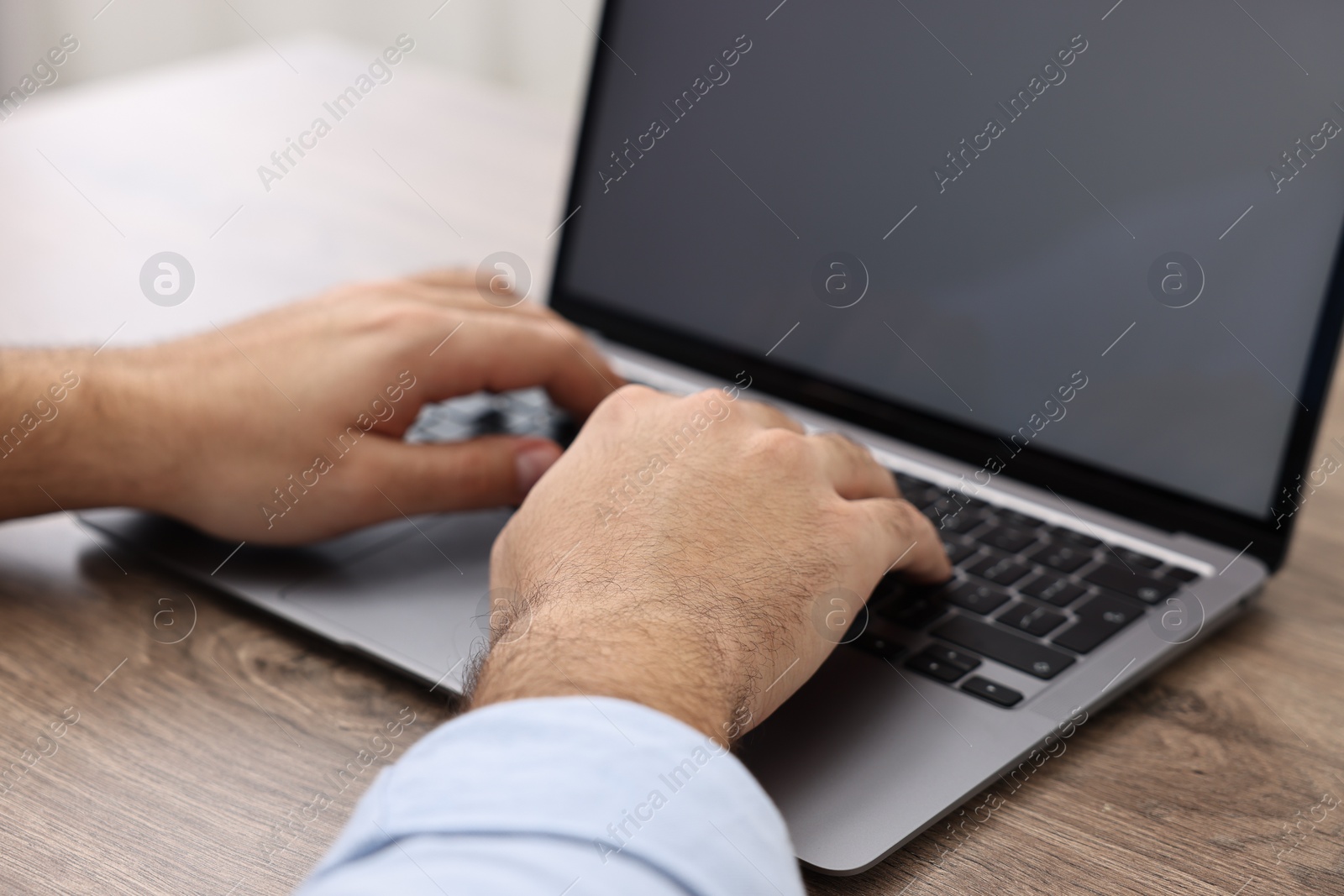 Photo of E-learning. Young man using laptop at wooden table, closeup