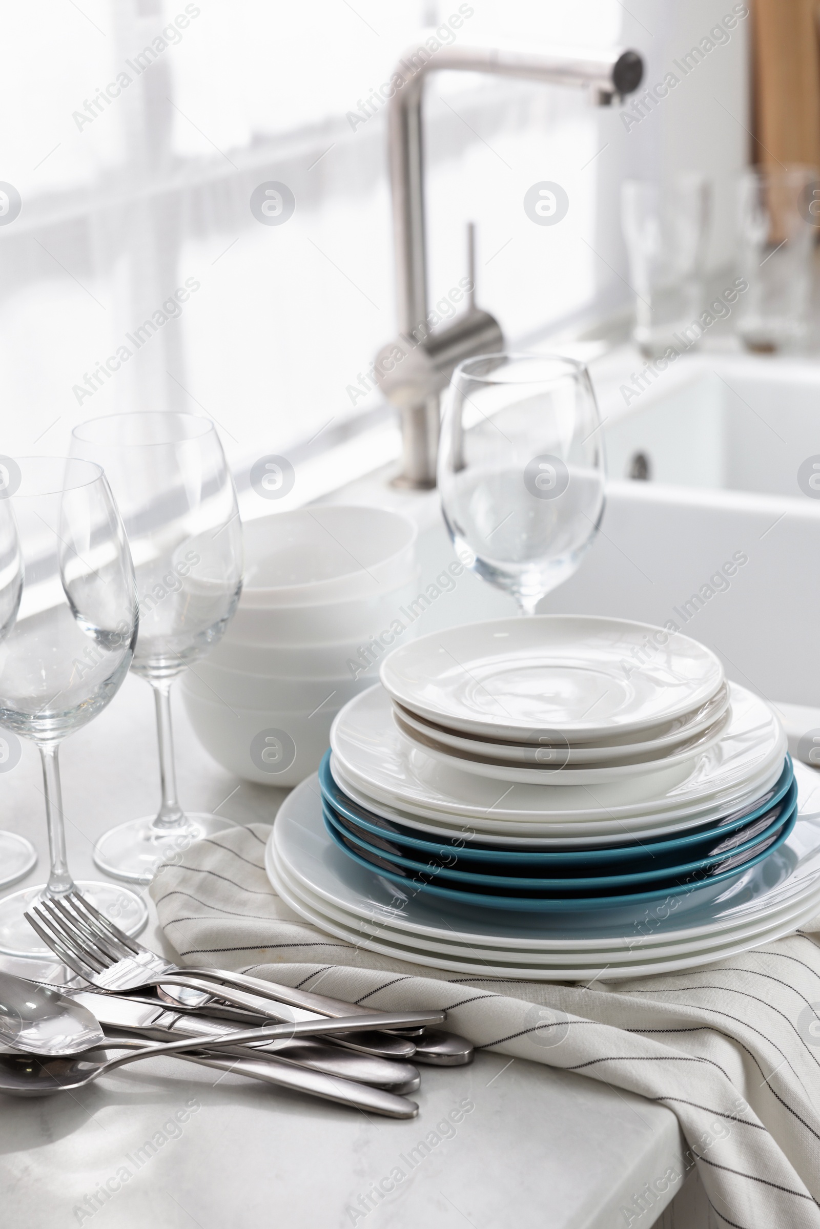 Photo of Different clean dishware, cutlery and glasses on countertop near sink in kitchen