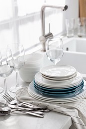 Photo of Different clean dishware, cutlery and glasses on countertop near sink in kitchen
