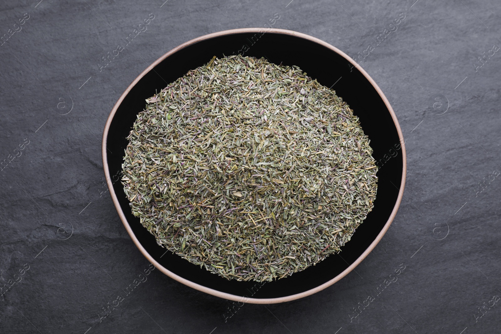 Photo of Bowl with dried thyme on black table, top view