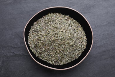 Bowl with dried thyme on black table, top view