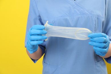 Photo of Doctor with unrolled female condom on yellow background, closeup. Safe sex