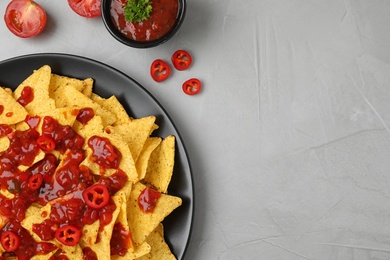 Plate of Mexican nacho chips with sauce on grey table, flat lay. Space for text