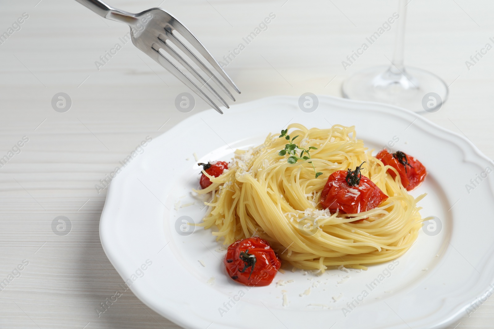 Photo of Eating tasty capellini with tomatoes and cheese at white wooden table, closeup. Exquisite presentation of pasta dish