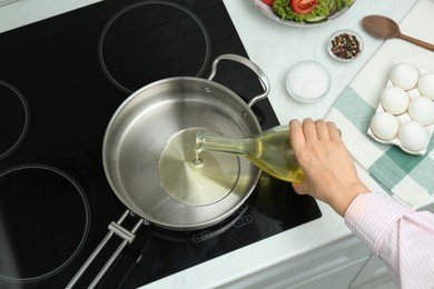 Photo of Woman pouring oil from jug into pan in kitchen, top view