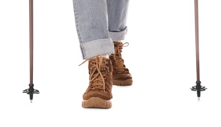 Woman wearing stylish hiking boots with trekking poles on white background, closeup
