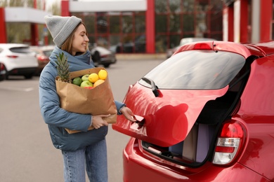 Photo of Young woman with bag of groceries near her car outdoors