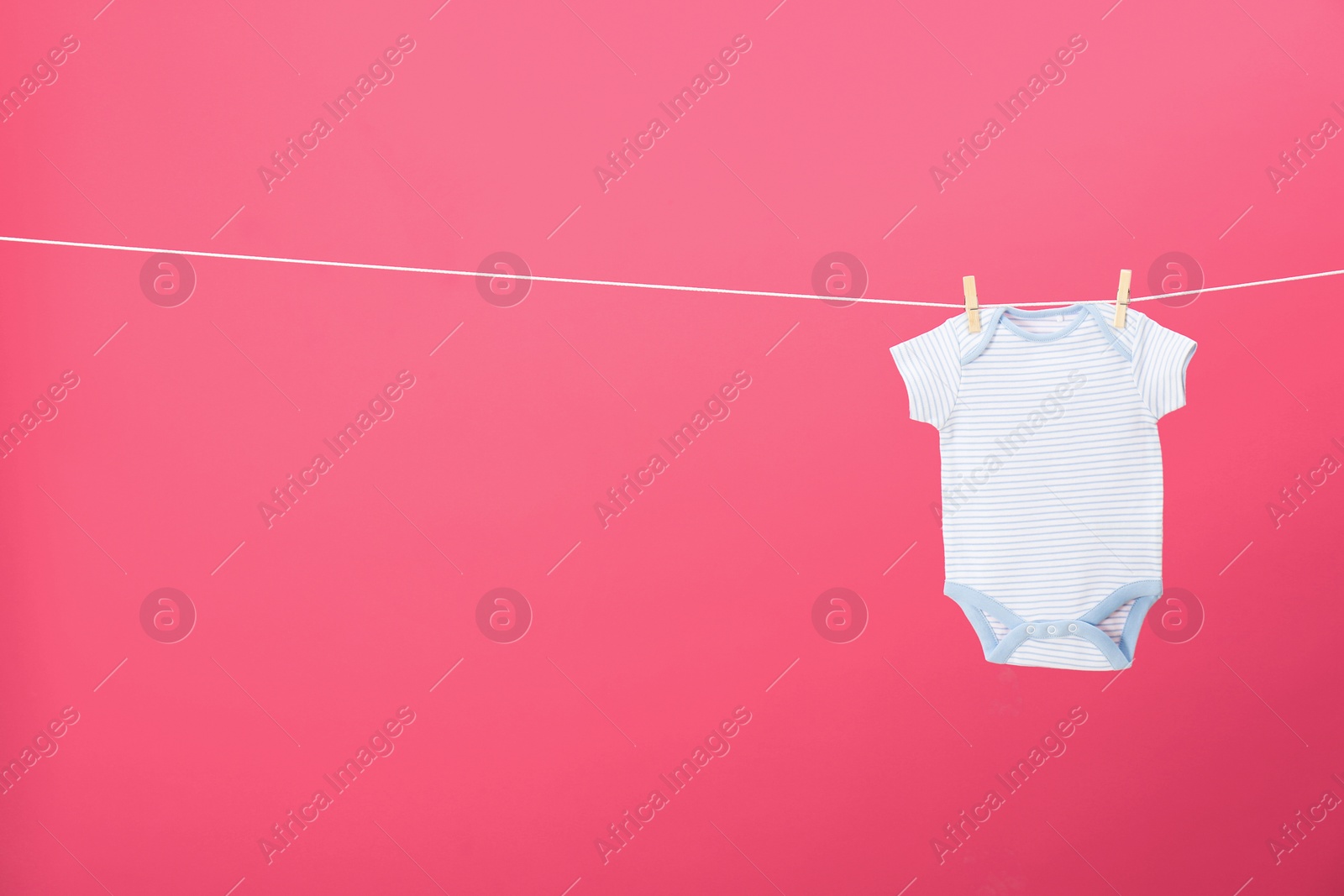 Photo of Baby onesie hanging on clothes line against pink background, space for text