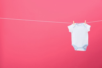 Photo of Baby onesie hanging on clothes line against pink background, space for text