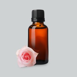 Image of Bottle of rose essential oil and flower on light grey background