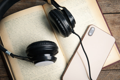Photo of Book, modern headphones and smartphone on wooden table, closeup