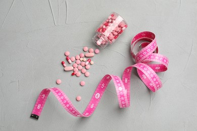 Photo of Jar of weight loss pills and measuring tape on grey table, flat lay