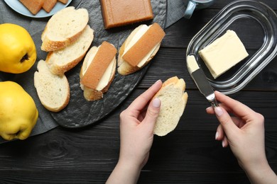 Photo of Making sandwich with quince paste. Woman spreading butter on bread at black wooden table, top view