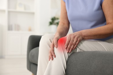 Image of Woman suffering from pain in knee on sofa indoors, closeup