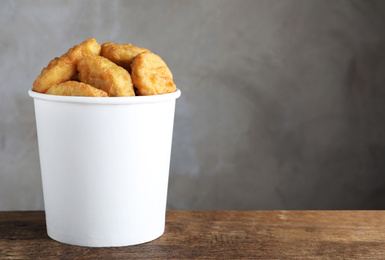 Photo of Bucket with delicious chicken nuggets on wooden table. Space for text