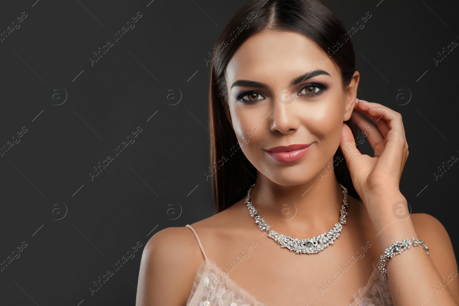 Photo of Beautiful young woman with elegant jewelry on dark background. Space for text