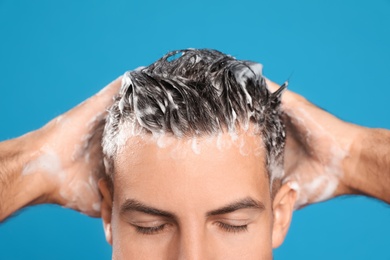 Photo of Handsome man washing hair on light blue background, closeup
