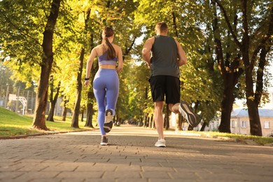 Photo of Sporty couple jogging in beautiful park on sunny day, back view