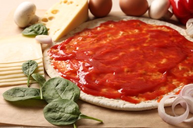 Photo of Pizza base smeared with tomato sauce and products on parchment, closeup