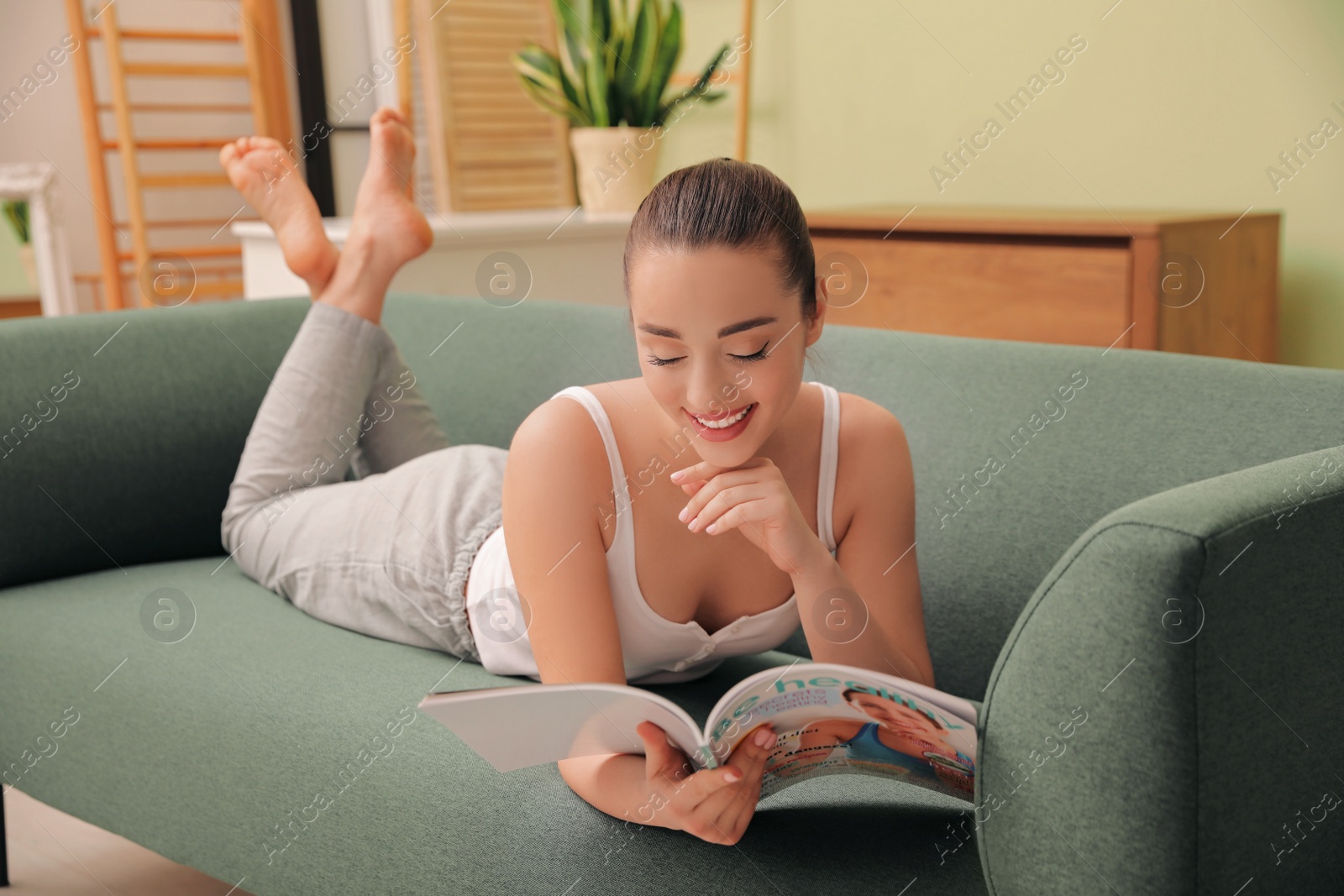 Photo of Happy woman reading magazine on sofa at home