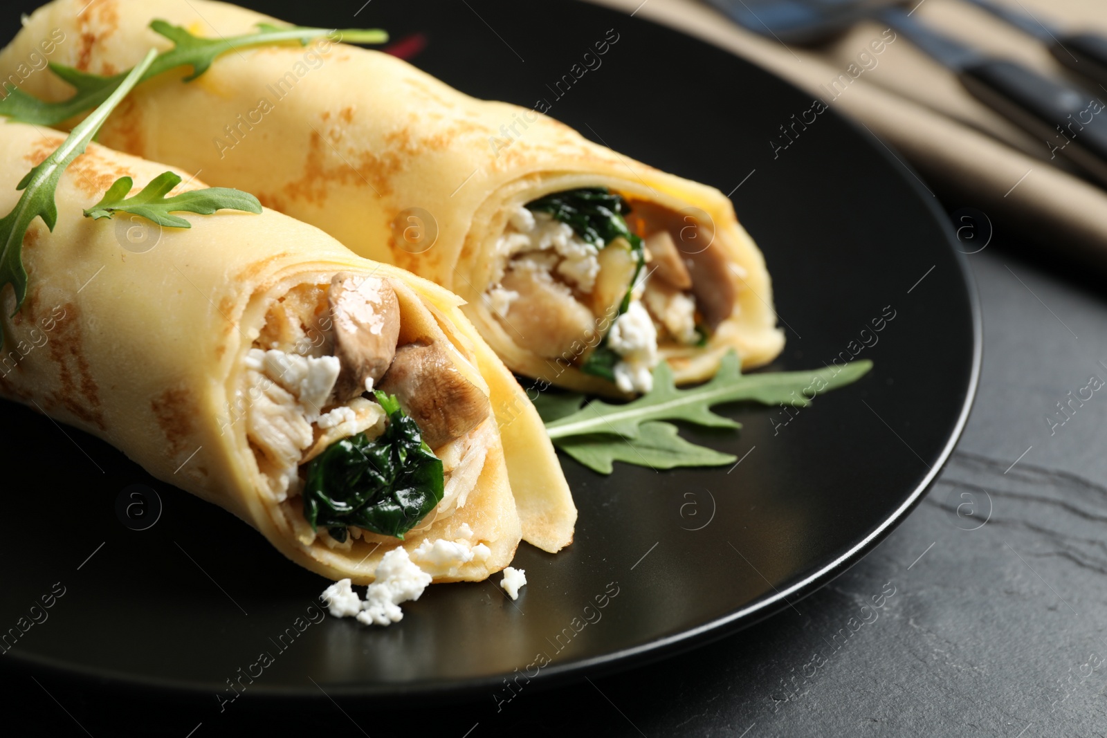 Photo of Delicious thin pancakes with chicken and mushrooms on black table, closeup