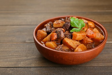 Delicious beef stew with carrots, parsley and potatoes on wooden table, closeup. Space for text