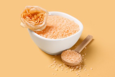 Photo of Bowl and spoon with sea salt, beautiful rose on yellow background