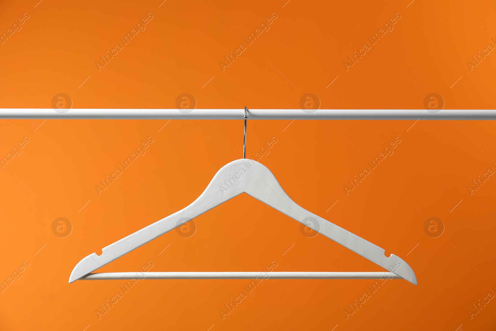 Photo of Empty clothes hanger on rack against orange background