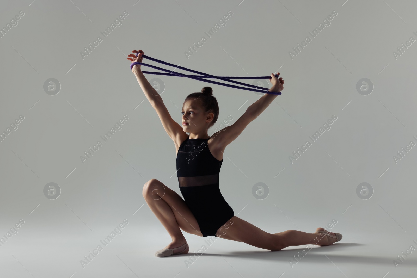 Photo of Cute little girl doing gymnastic exercise with rope on white background