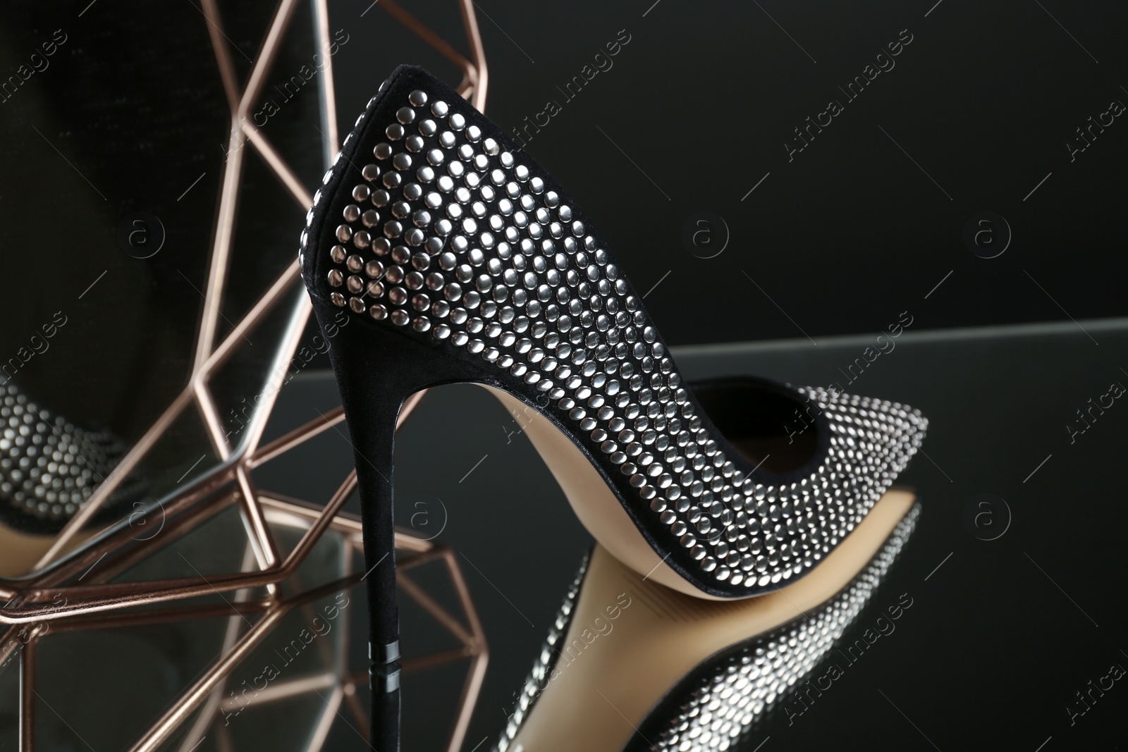 Photo of Stylish high heel shoe on mirror surface against dark background