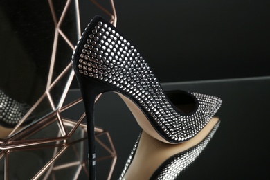 Photo of Stylish high heel shoe on mirror surface against dark background