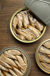 Open tin cans of sprats on wooden table, flat lay