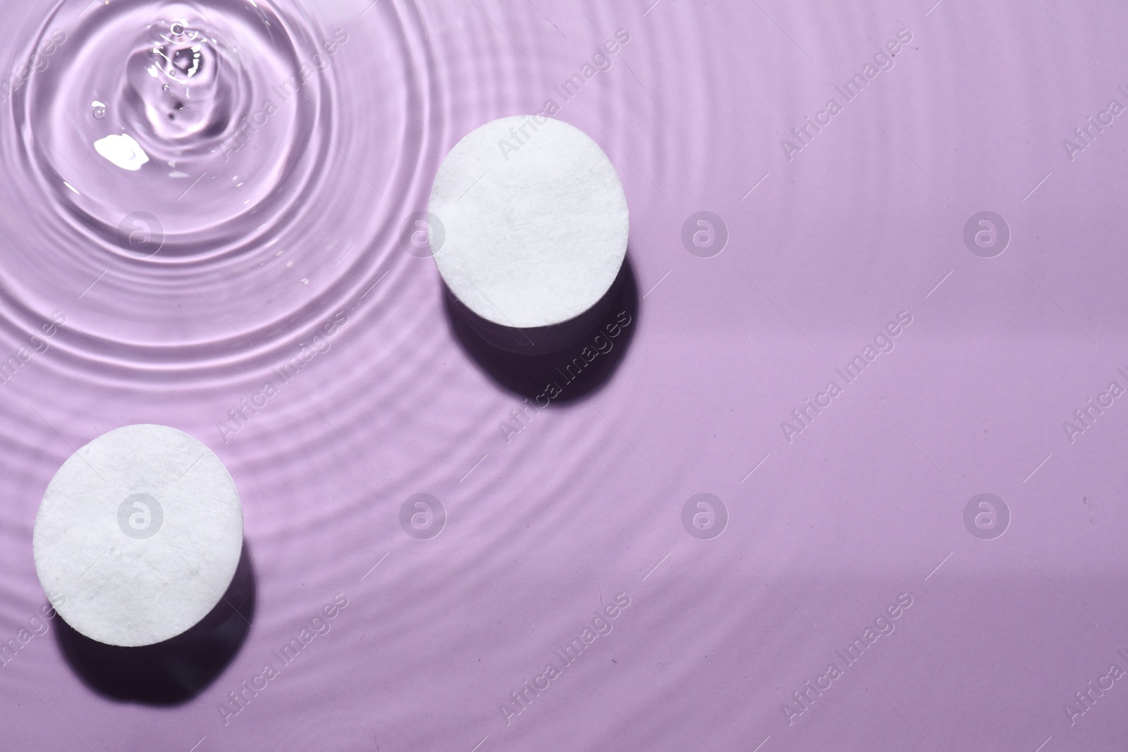 Photo of Cotton pads in micellar water on violet background, top view. Space for text