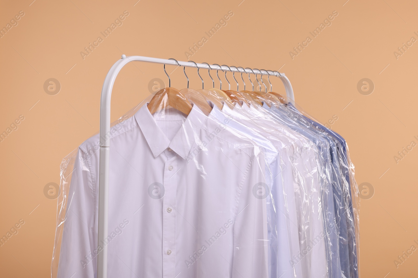 Photo of Dry-cleaning service. Many different clothes in plastic bags hanging on rack against beige background