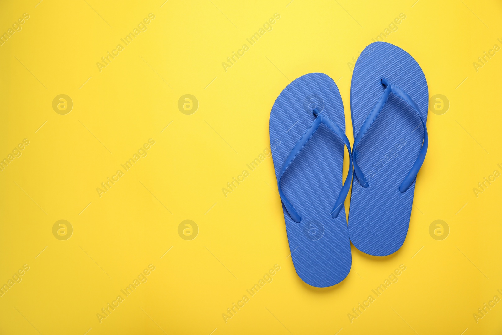 Photo of Stylish blue flip flops on yellow background, top view. Space for text