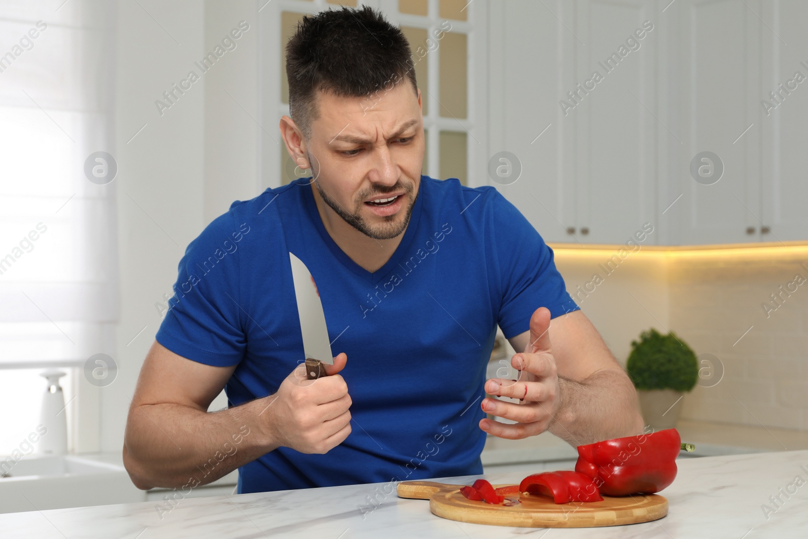 Photo of Man cut finger with knife while cooking at white marble table in kitchen