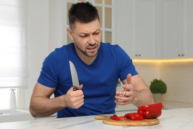 Photo of Man cut finger with knife while cooking at white marble table in kitchen