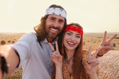 Photo of Happy hippie couple showing peace signs while taking selfie in field