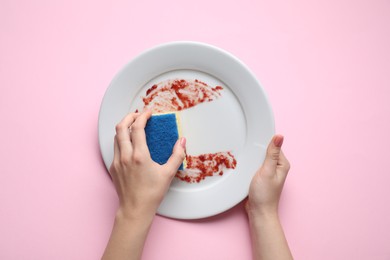 Woman washing dirty plate with sponge on pink background, top view