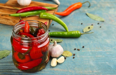 Photo of Glass jar of pickled chili peppers on light blue wooden table. Space for text