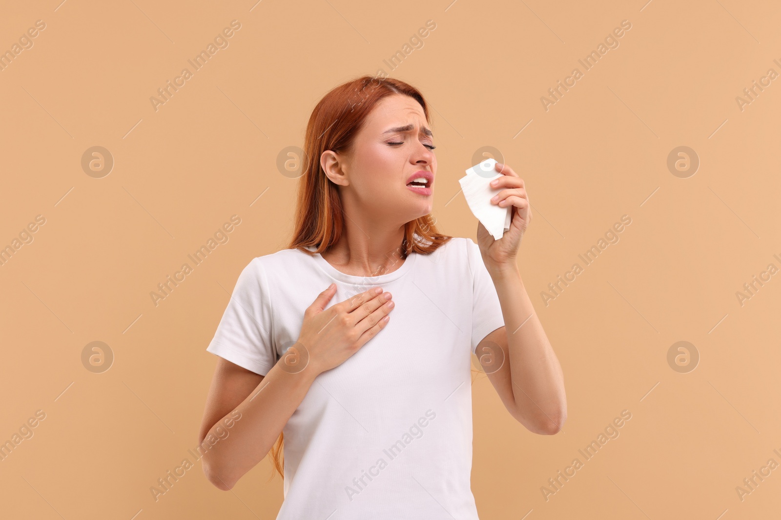 Photo of Suffering from allergy. Young woman with tissue sneezing on beige background