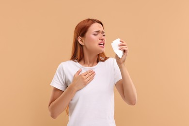 Photo of Suffering from allergy. Young woman with tissue sneezing on beige background