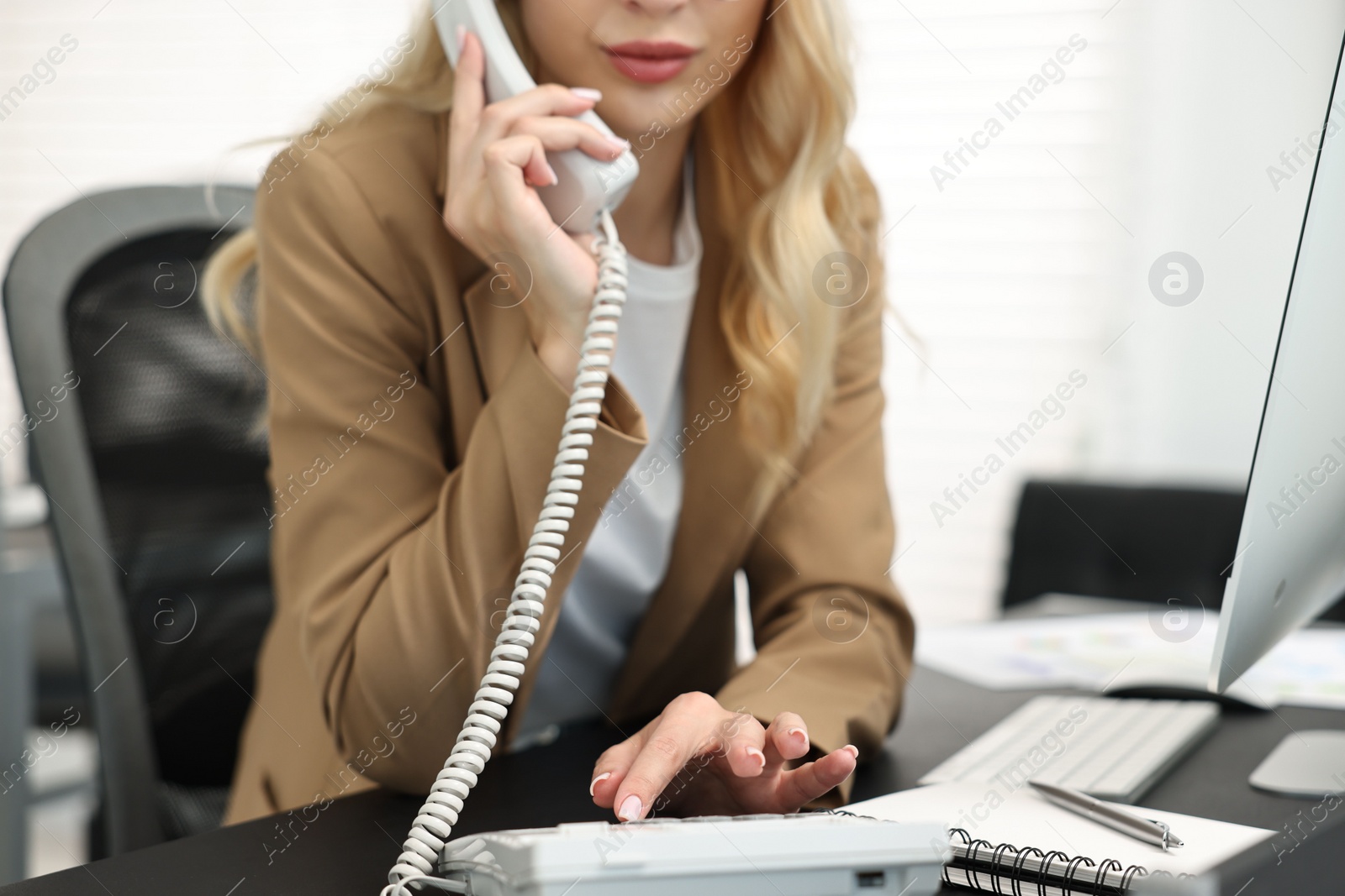 Photo of Secretary talking on phone at table in office, closeup