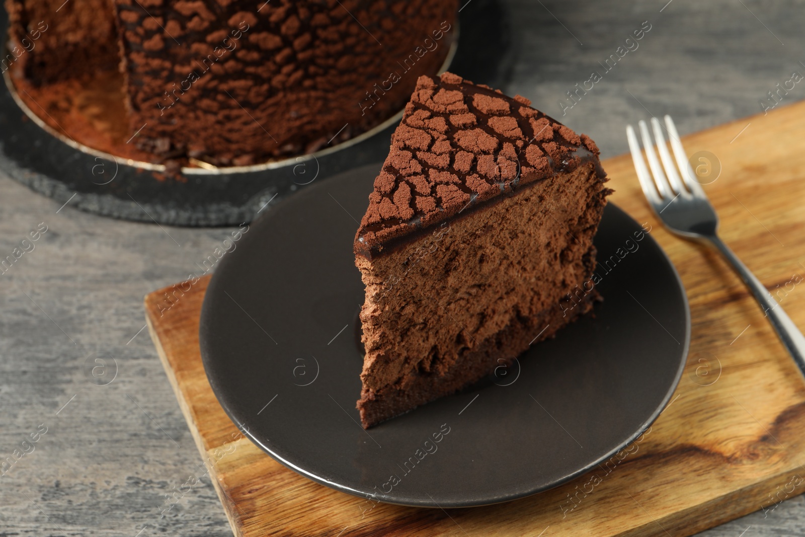 Photo of Piece of delicious chocolate truffle cake on grey textured table, closeup