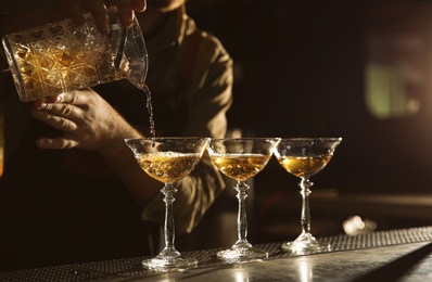 Photo of Barman pouring cold martini into glasses on counter, closeup. Space for text