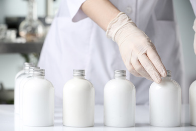 Scientist with bottles of cosmetic product in laboratory, closeup
