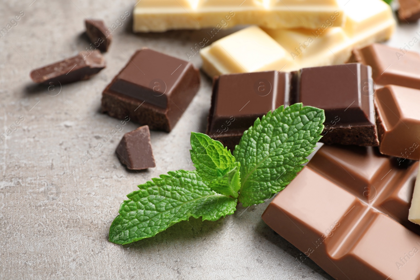 Photo of Different kinds of chocolate with mint on gray table